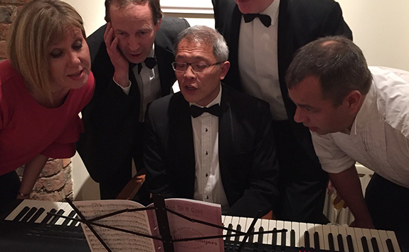 Alumni singing around a piano together